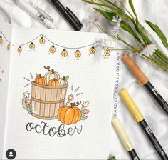 an open notebook with pumpkins on the cover and markers next to it, along with some flowers