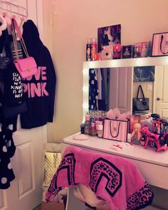 a pink and black vanity in a girls room with clothes hanging on the rack, mirror and purses