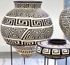 two black and white vases sitting next to each other on metal stands in front of a wall