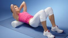 a woman in pink shirt and white pants doing exercises on blue mat with foam rollers