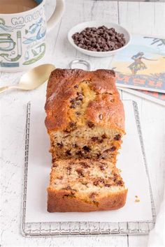 a loaf of chocolate chip banana bread sitting on top of a cooling rack next to a cup of coffee