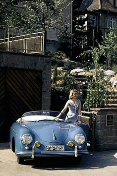 a woman sitting on the hood of a blue sports car in front of a house