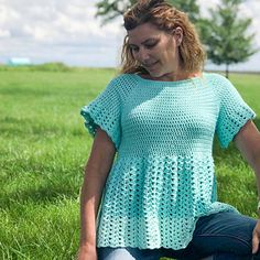 a woman sitting in the grass wearing a blue crochet top