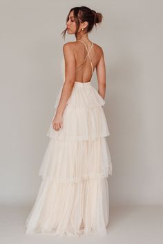 the back of a woman wearing a white dress with tiered layers and open straps