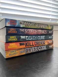 a stack of five books sitting on top of a wooden table next to a window