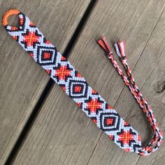 an orange, white and black beaded lanyard on a wooden surface