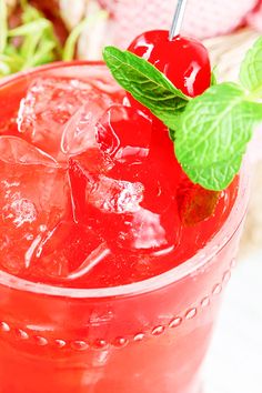 a close up of a drink with ice and cherries on the rim, garnished with a green leaf