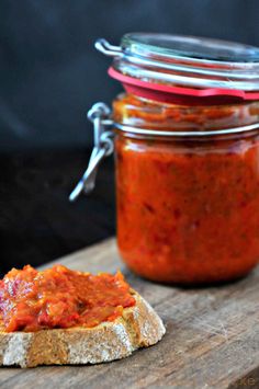 a jar of red sauce sitting on top of a wooden table next to a piece of bread