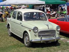 two old cars parked next to each other in the grass near tents and people on bikes