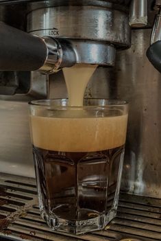 an espresso machine is filling a glass with liquid