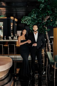 a man and woman standing next to each other in front of a table with chairs