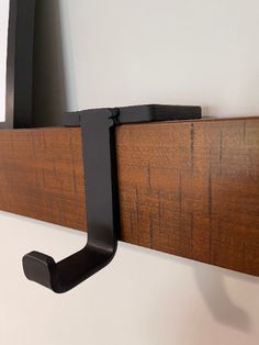 a wooden shelf with a black metal hook on it's side and a mirror in the background