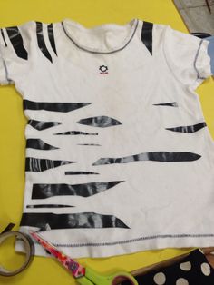 a white t - shirt with black and white designs on it next to some scissors