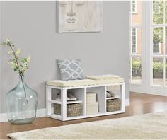 a white bench with baskets underneath it and a vase on the floor next to it