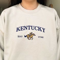 *SIZES ARE UNISEX* -I'd suggest your usual size for a more fitted look, or sizing up for a more relaxed fit. *these sweatshirts are extra comfy when oversized "Kentucky" and a horse embroidered on a comfy vintage-style crewneck. A sturdy and warm sweatshirt bound to keep you warm in the colder months. A pre-shrunk, classic fit sweater that's made with air-jet spun yarn for a soft feel and reduced pilling. Your new favorite sweatshirt! * 50% cotton, 50% polyester * Pre-shrunk * Classic fit with no center crease * 1x1 athletic rib knit collar with spandex * Air-jet spun yarn with a soft feel and reduced pilling * Double-needle stitched collar, shoulders, armholes, cuffs, and hem * Gildan 18000 Unisex Heavyblend Sweatshirt Please note that the embroidery comes with a backing that acts as a st Collegiate Crew Neck Top With Embroidered Logo, Collegiate Crew Neck Top With Embroidered Graphics, Varsity Crew Neck Tops With Embroidered Graphics, Fitted Crew Neck Casual Sweatshirt, Casual Fitted Crew Neck Sweatshirt, Retro Tops With Embroidered Graphics For Winter, Vintage Cotton Tops With Letter Embroidery, Vintage Long Sleeve Tops With Embroidered Text, Retro Crew Neck Sweatshirt With Embroidered Graphics