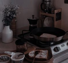 black and white photograph of food cooking on stove top with flowers in vase next to it