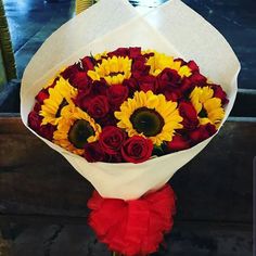 a bouquet of sunflowers and red roses wrapped in white paper on a table