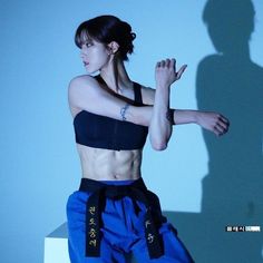 a woman in blue pants and black bra top posing with her arms stretched out to the side