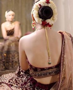 the back of a woman's head with flowers in her hair and an elaborate necklace