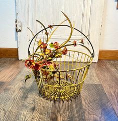 a metal basket with flowers in it sitting on the floor next to a white door