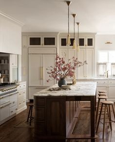 a kitchen with white cabinets and marble counter tops, an island in the middle is surrounded by bar stools