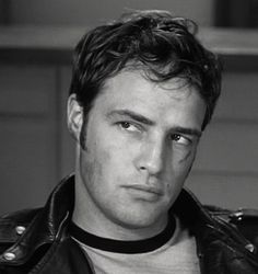 a man wearing a black leather jacket and white t - shirt is looking at the camera