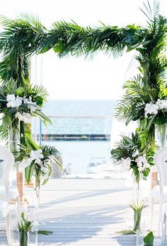 an outdoor ceremony setup with white chairs and greenery on the aisle, overlooking the ocean