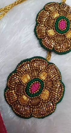 pair of gold and green beaded earrings on white furnishing with red ribbon