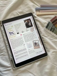 a tablet computer sitting on top of a bed next to some books and pencils