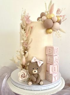 a baby shower cake with a teddy bear next to it and flowers on the side