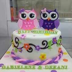 two owls sitting on top of a white cake with purple and green frosted decorations