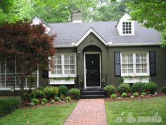 a green house with white windows and black shutters on the front door is shown