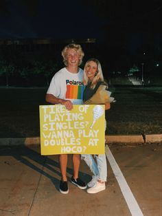 two people standing in a parking lot holding a sign