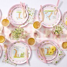 a table set with pink and white plates, spoons, forks and utensils