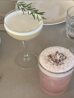 two cocktails sitting on top of a table next to plates and utensils