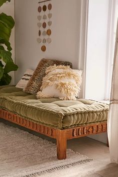 a couch with pillows on top of it in front of a window next to a potted plant