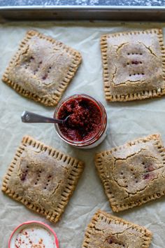 small crackers with jam on them sitting on a baking sheet next to a cup of sauce