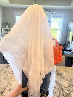 a young child standing on top of a counter next to a white sheet over his head