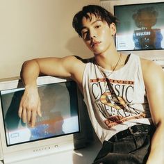 a young man sitting in front of a computer monitor with his arm on the desk