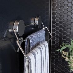 a towel rack holding two towels and a potted plant in front of a black wall