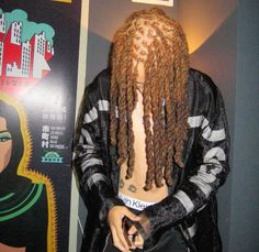 a man with dreadlocks is standing in front of a poster and holding a purse