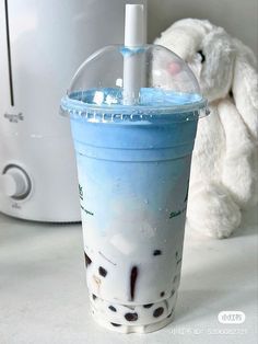 a blue drink in a plastic cup next to a stuffed animal