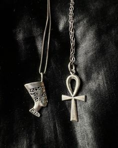 two silver necklaces with an egyptian cross and anub on one side, sitting on a black surface