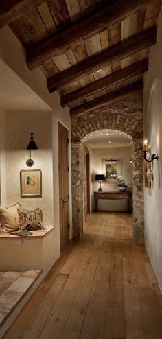 a long hallway with wooden floors and stone walls is lit by two lights on either side of the room