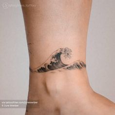 a woman's foot with a wave tattoo on the side of her leg and an ocean wave behind it