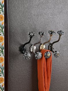 an orange scarf hanging on the wall next to some metal knobs and hooks with flowers