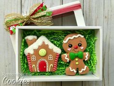 two gingerbread cookies in a box with green grass and bows on the top one is decorated like a ginger