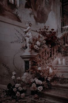 flowers and candles are on the steps in front of a wall with an angel statue