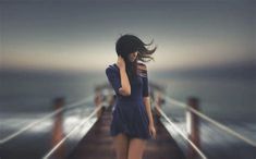 a woman walking down a pier next to the ocean with her hair blowing in the wind