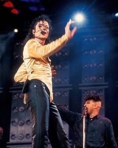 michael jackson performing on stage with his hands in the air while another man stands behind him